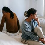 Woman sitting on bed looking sadly away from man sitting on bed