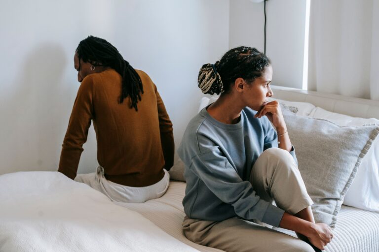 Woman sitting on bed looking sadly away from man sitting on bed